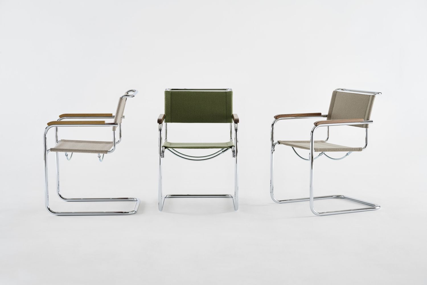 Drei Stahlrohr-Freischwingerstühle mit Holz- und Stoffdetails, einer in Grün, zwei in Beige, auf weißem Hintergrund.