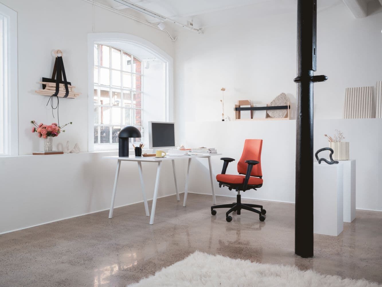 Modernes Büro mit rotem ergonomischen Stuhl, weißem Schreibtisch, Computer und stilvoller Dekoration in hellem Raum.