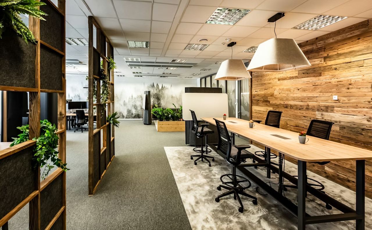 Modernes Büro mit ergonomischen Stühlen, Holzwand, Pflanzen und großem Besprechungstisch unter stilvollen Lampen.