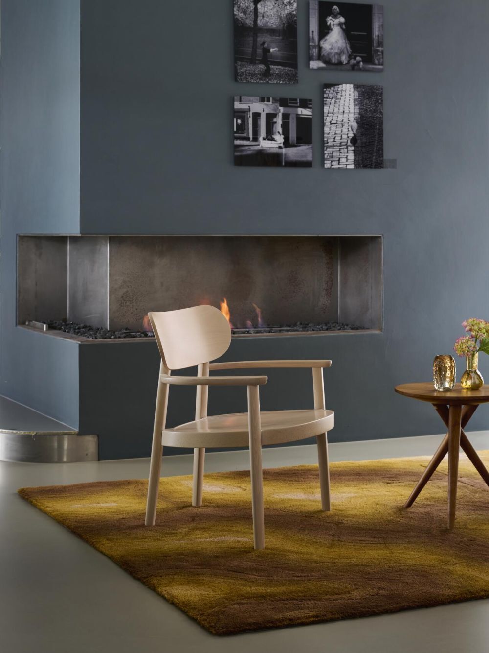 Minimalistischer Holzstuhl vor Kamin, umgeben von modernem Interieur und Kunst an der Wand.