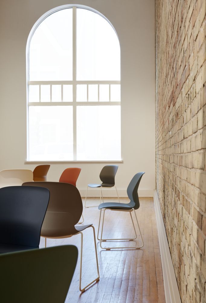 Moderne ergonomische Stühle in einem Raum mit großen Fenstern und sichtbarer Ziegelwand.
