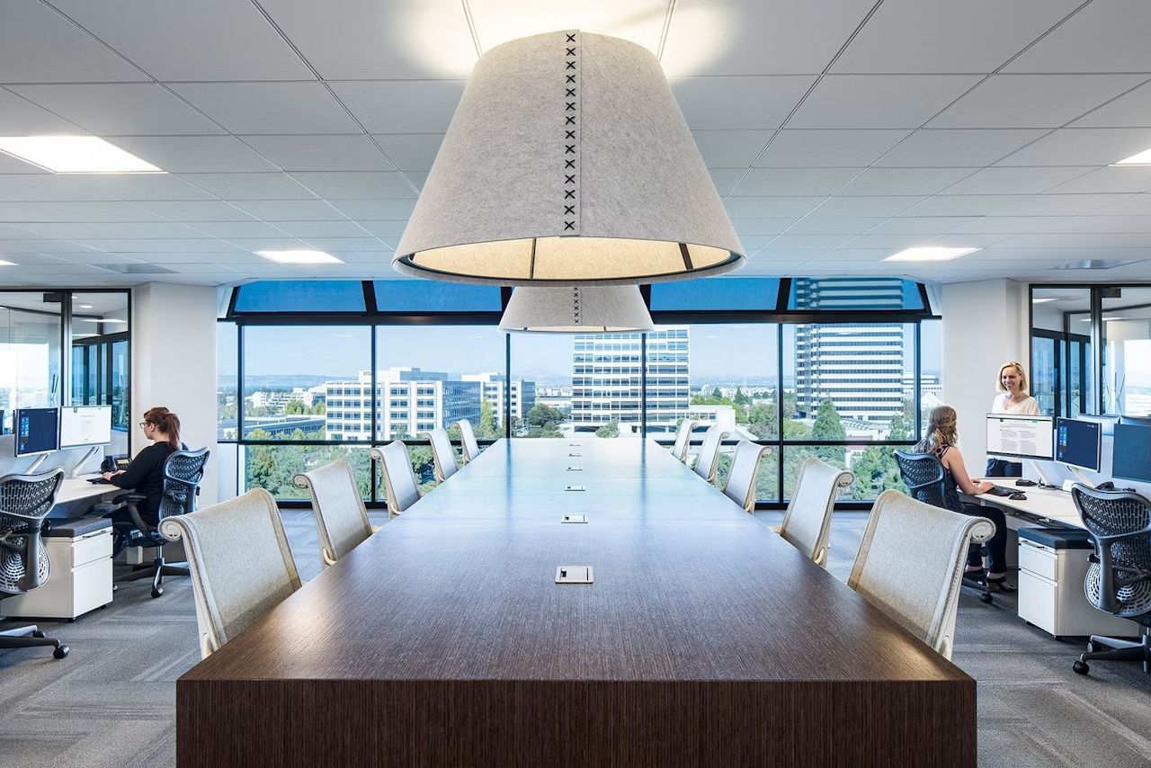 Moderne Büroumgebung mit ergonomischen Stühlen, großzügigen Fenstern und Mitarbeitern an Computern in einer Büroetage.