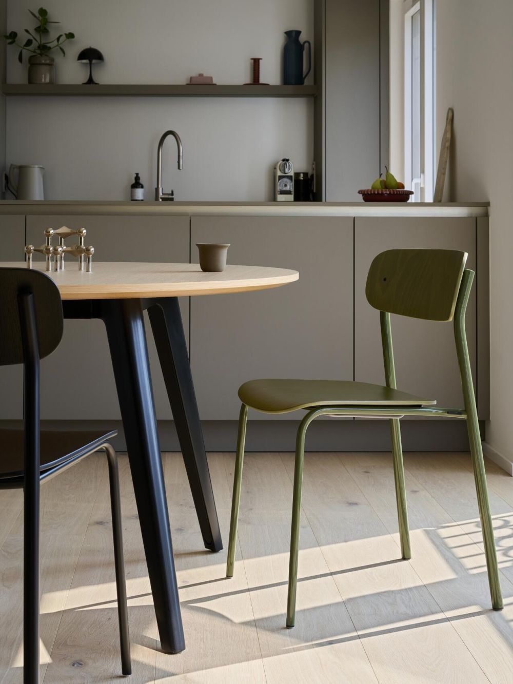 Moderner Essbereich mit Holzstuhl, rundem Tisch und minimalistischer Küche im Hintergrund.