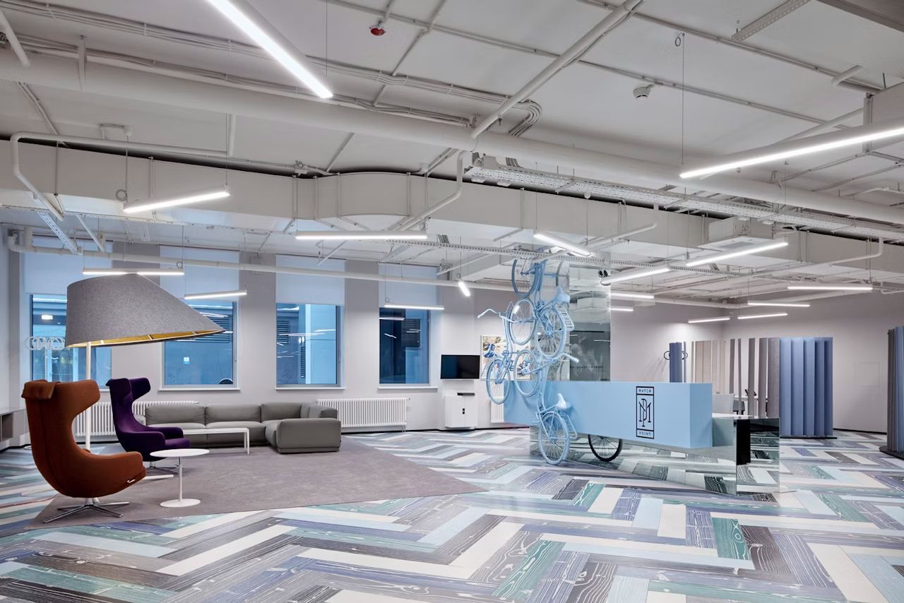 Modernes Büro mit ergonomischen Stühlen, großer Sofa-Sitzgruppe, hängenden Fahrrädern und auffälliger Beleuchtung.