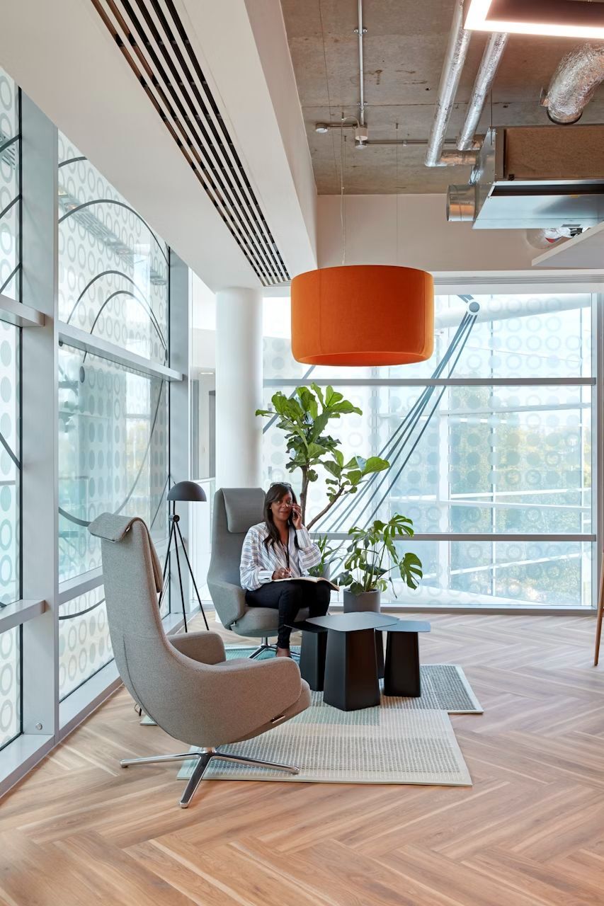 Frau sitzt in einem modernen, ergonomischen Bürostuhl in einem hellen Büro mit Pflanzen und stilvoller Einrichtung.