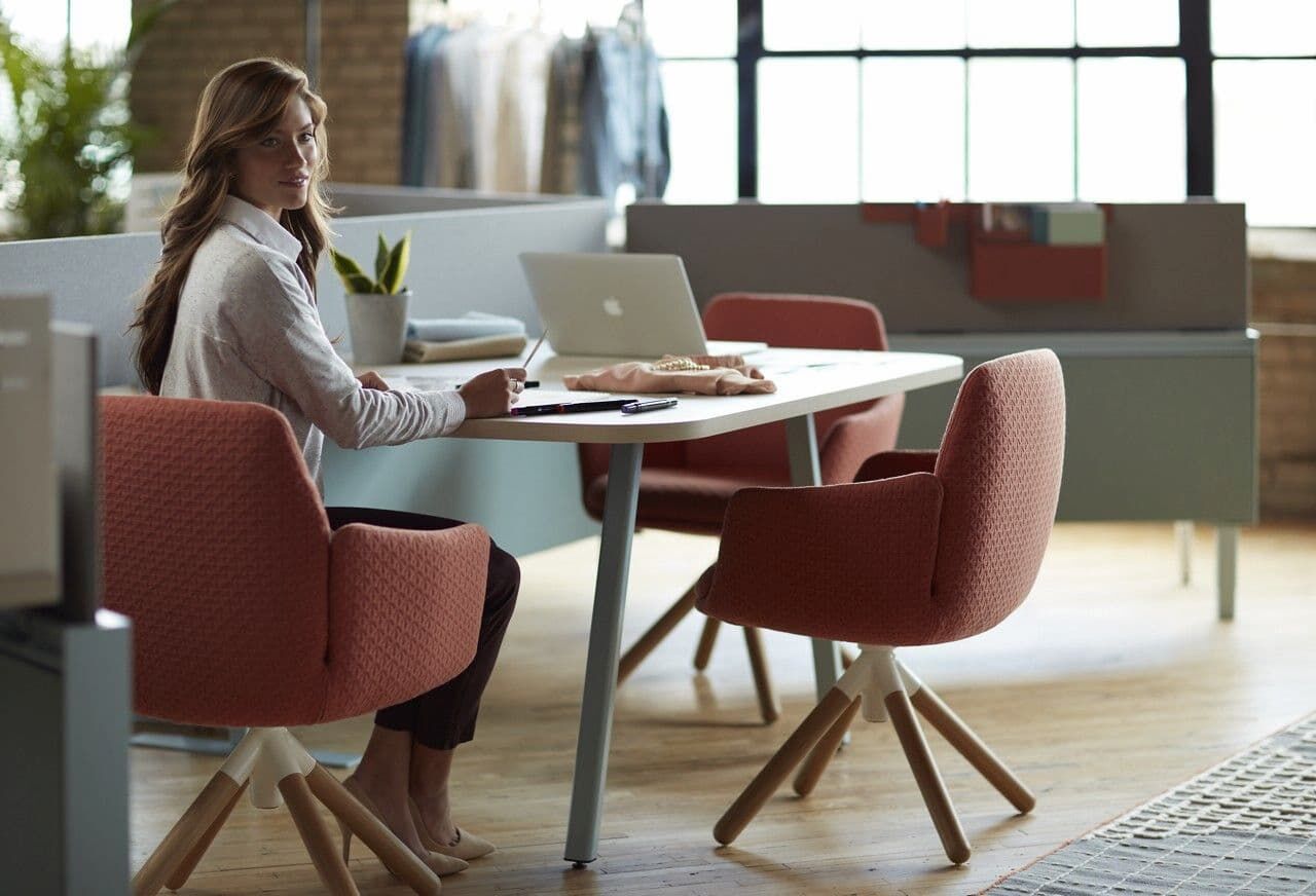 Frau sitzt an modernem Schreibtisch mit ergonomischem Stuhl, Laptop und stilvollem Büroambiente im Hintergrund.