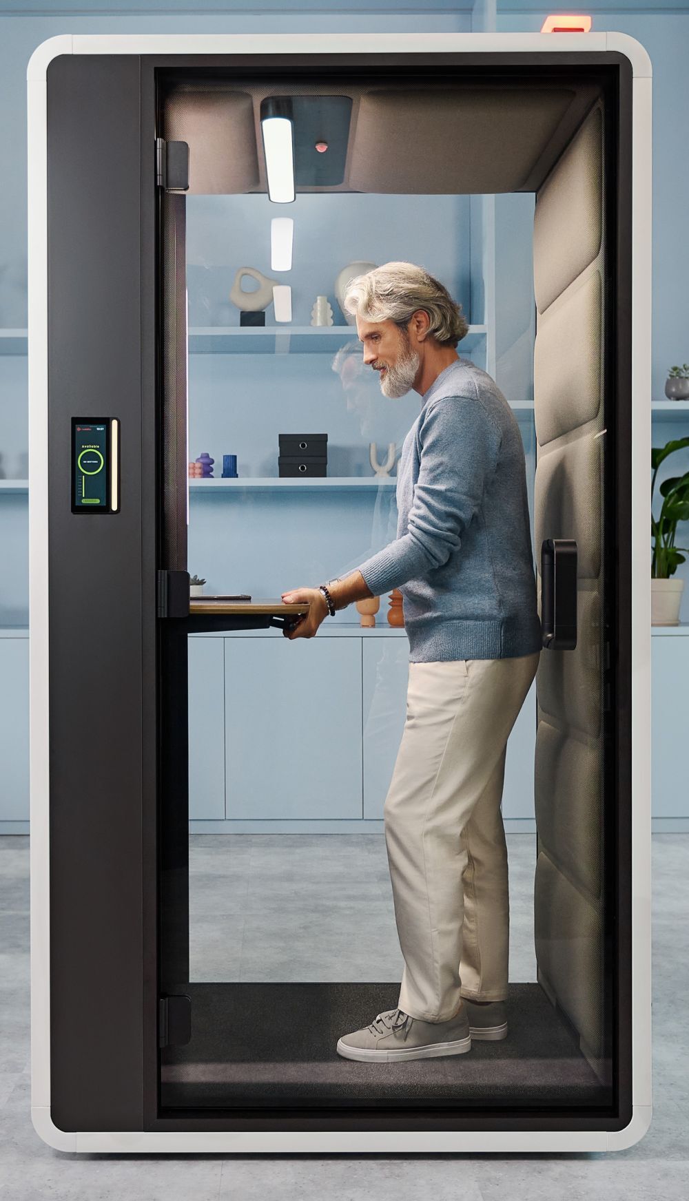 Ein Mann in einer schallisolierten Kabine steht an einem Stehpult, in einem modernen Büroambiente.