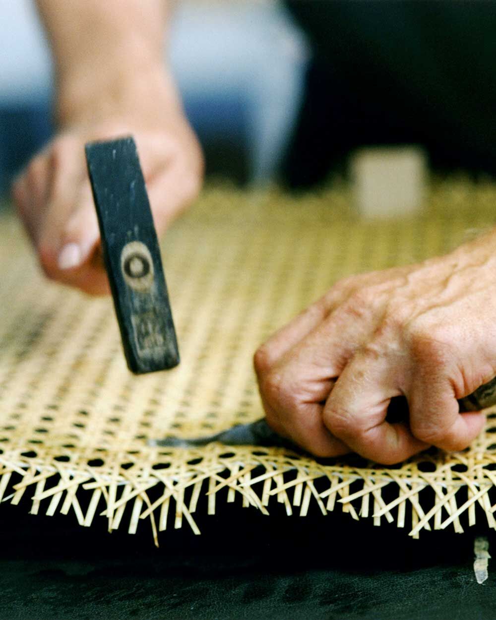 Nahaufnahme von Händen, die Rattan für einen ergonomischen Stuhl flechten, betont handwerkliche Qualität.