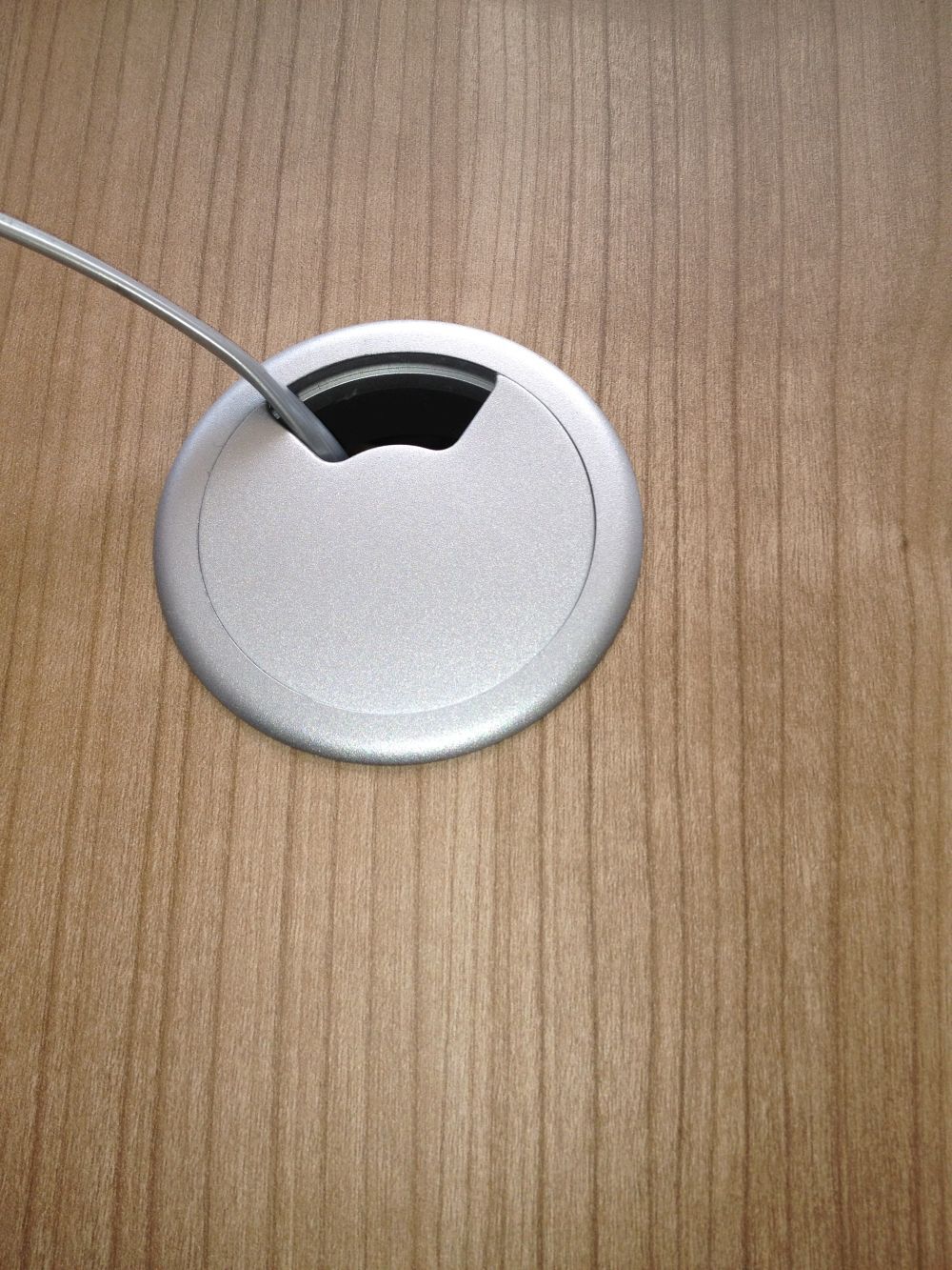 Runder Kabeldurchlass auf einem Holztisch, der ein Kabel ordnet und verbirgt.
