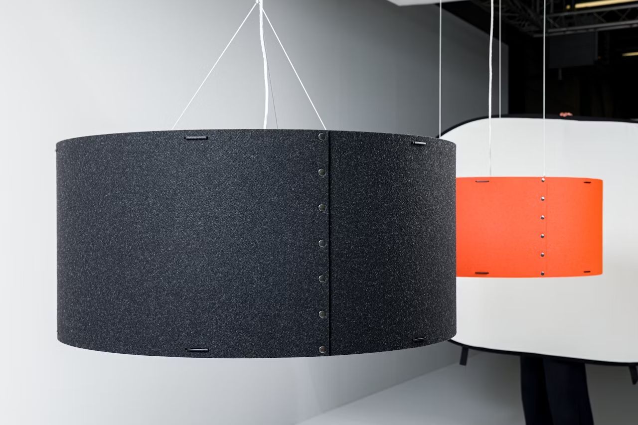 Zwei hängende akustische Paneele, eines in Schwarz, das andere in Orange, vor einem neutralen Hintergrund.