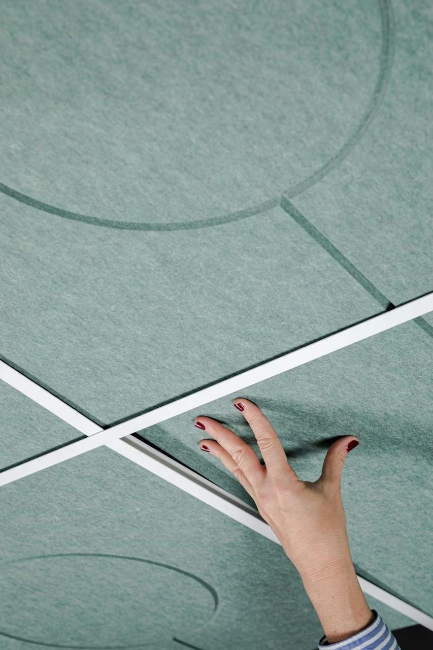 Hand berührt akustische Deckenplatte mit kreisförmigen Mustern in einem modernen Bürodesign.