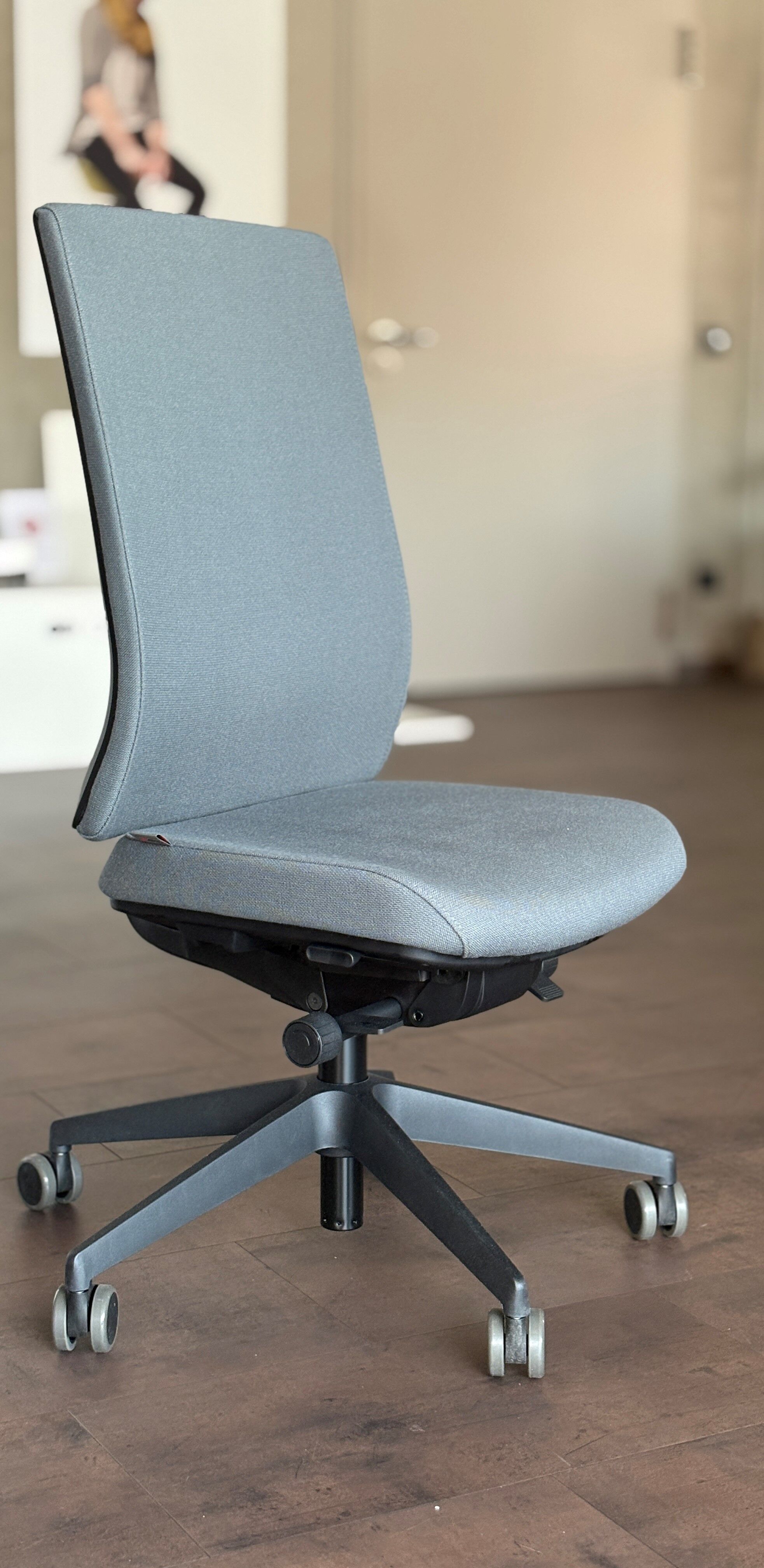 Moderner ergonomischer Bürostuhl mit grauem Stoff, verstellbarer Rückenlehne und Rollen für dynamisches Sitzen.