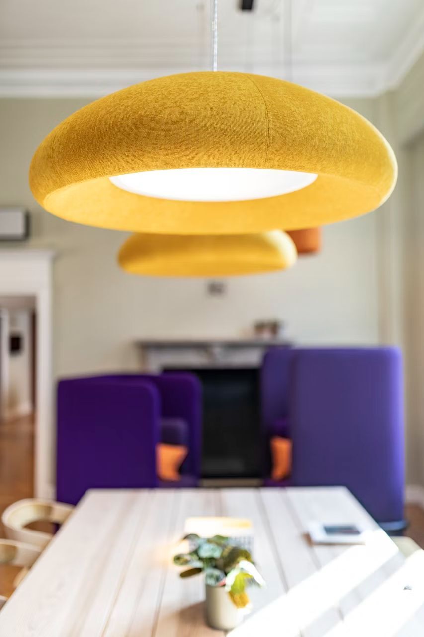 Moderne gelbe Pendelleuchten hängen über einem Tisch, im Hintergrund lila Sessel in einem stilvollen Raum.