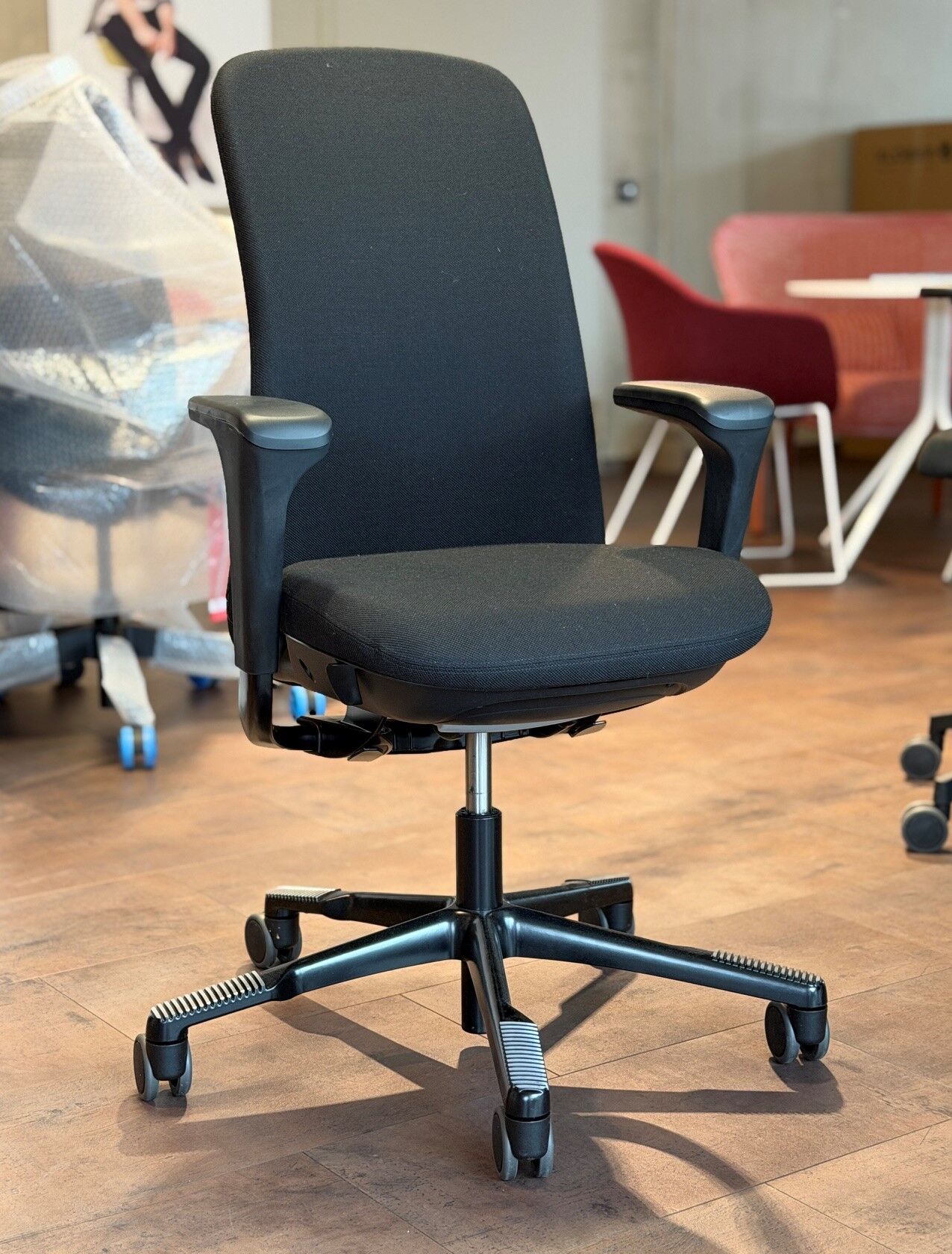 Schwarzer ergonomischer Bürostuhl mit Armlehnen auf Holzfußboden, ideal für gesundes und dynamisches Sitzen.