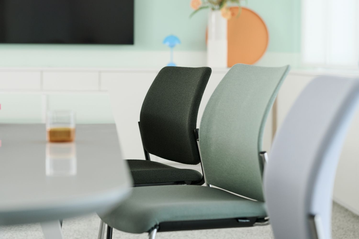 Ergonomische Bürostühle in modernem Design vor einem Konferenztisch, im Hintergrund dekorative Wanddetails.