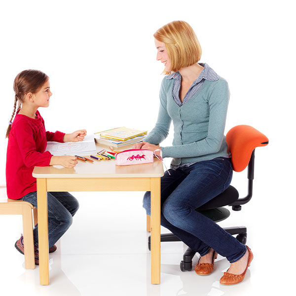 Erzieherin sitzt auf einem Erzieherstuhl mit niedriger Sitzhöhe am Tisch mit einem Kind und spielt