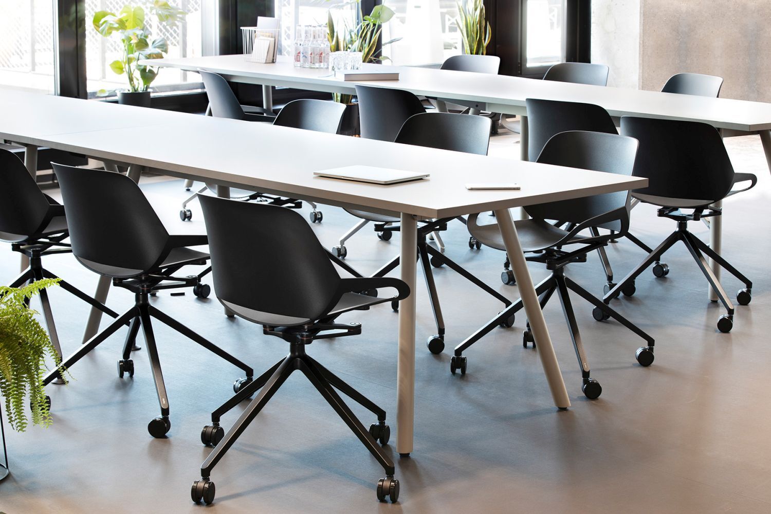 Moderne Büroräume mit ergonomischen Drehstühlen und großen Tischen, fördernd für dynamisches Sitzen.