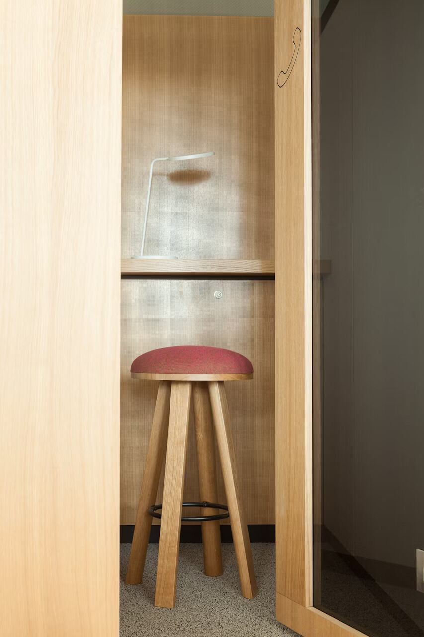 Hochstuhl mit rotem Sitzpolster und weißer Lampe in einer Holzkabine.