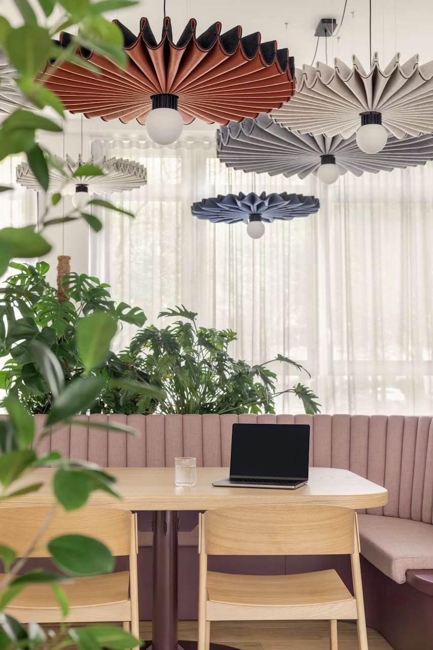 Moderne Büroeinrichtung mit Laptop auf Tisch, Holzstühle, bunte Lampen und Pflanzen im Hintergrund.