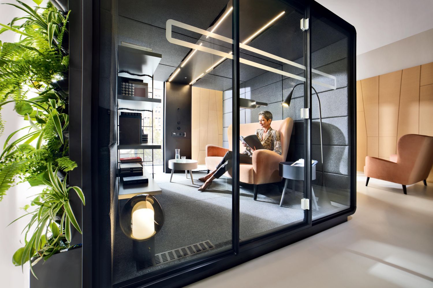 Person sitzt entspannt in einer modernen, schallisolierten Kabine mit ergonomischem Stuhl und Pflanzen.