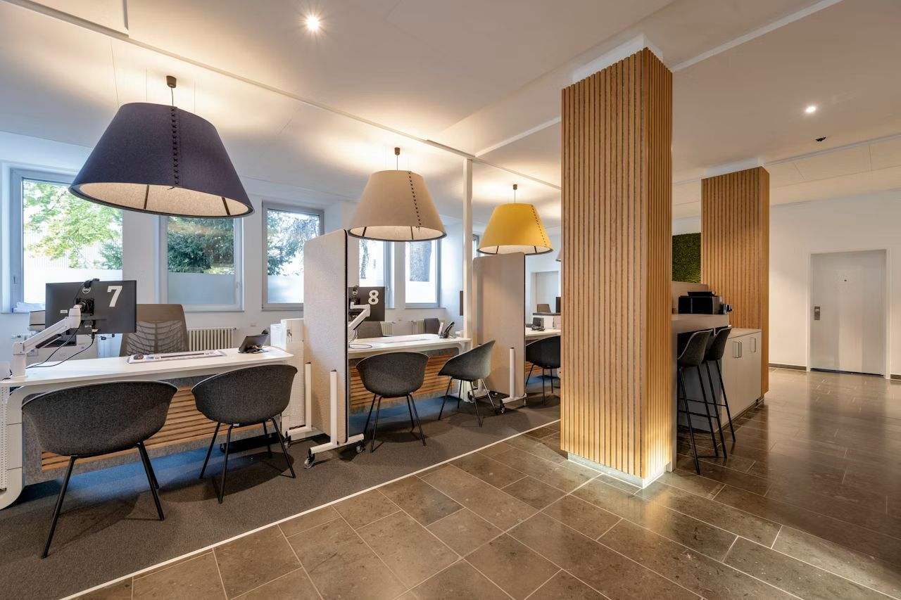 Modernes Büro mit ergonomischen Arbeitsplätzen, stilvollen Lampen und Schreibtischen, die dynamisches Sitzen unterstützen.