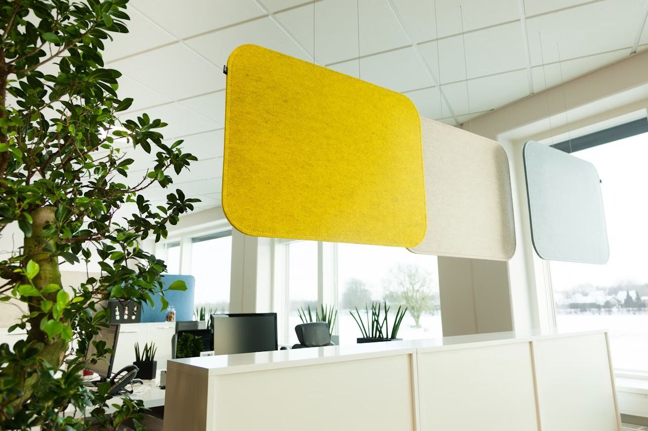 Moderne Büroeinrichtung mit hängenden Akustikpaneelen in Gelb, Beige und Blau in einem hellen Raum.