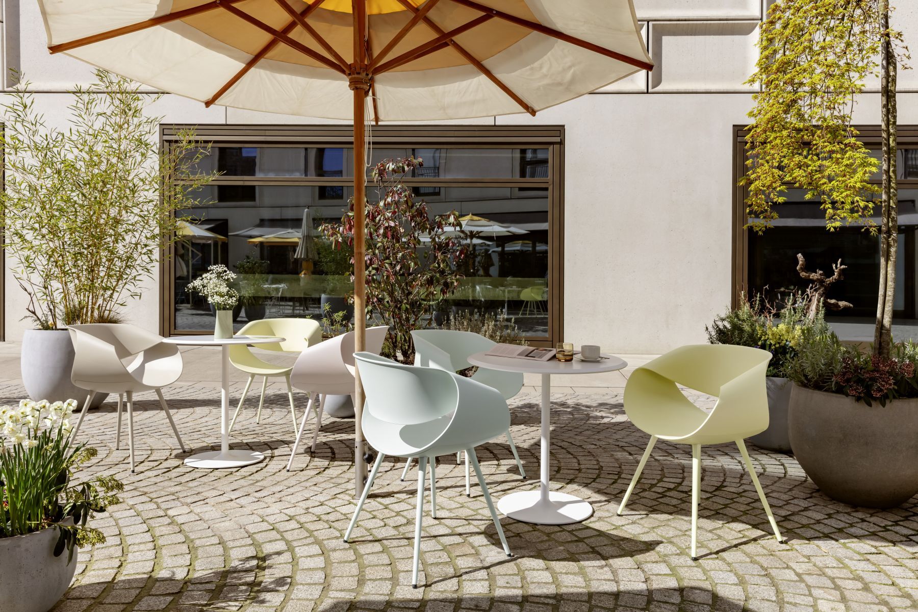 Moderne Terrassenstühle unter einem Sonnenschirm, umgeben von Pflanzen in Töpfen, ideal für den Außenbereich.