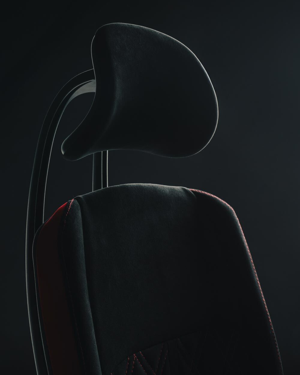 Nahaufnahme eines ergonomischen Bürostuhls mit Kopfstütze und subtilen roten Nähten auf dunklem Hintergrund.