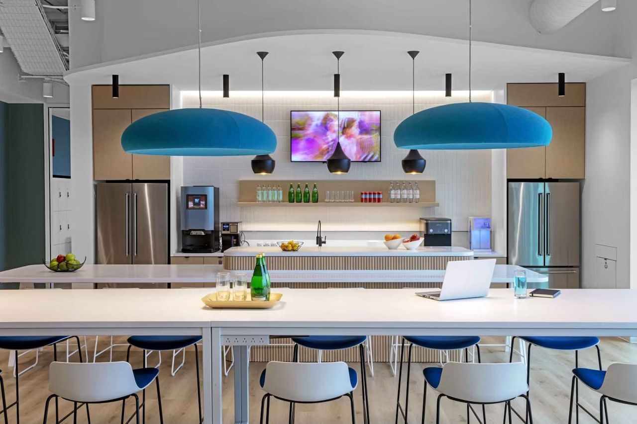 Moderne Büroküche mit Barhockern, Edelstahlgeräten und großen blauen Hängeleuchten.