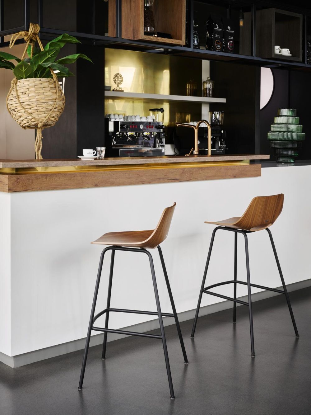 Moderne Barstühle aus Holz und Metall vor einer stilvollen Küchentheke mit Kaffeemaschine und hängendem Pflanzenkorb.
