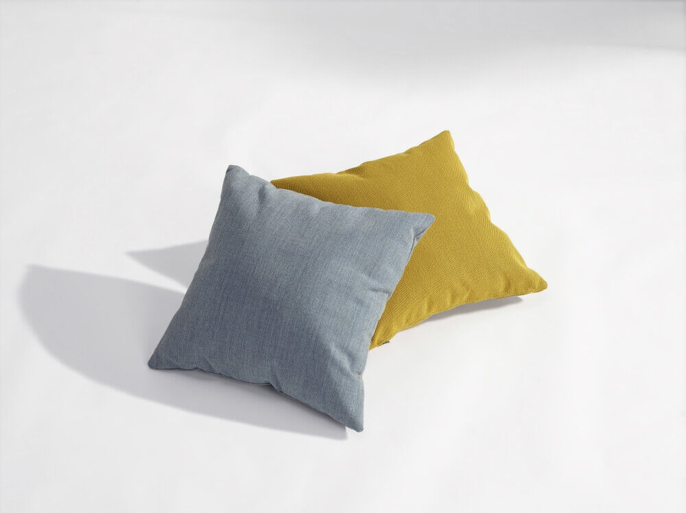 Zwei Kissen, eines blau und eines gelb, liegen aufeinander auf einem hellen Hintergrund.