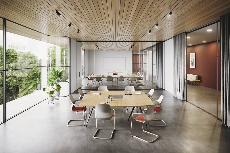 Modernes Büro mit ergonomischen Stühlen und Holztisch, großer Fensterfront und grüner Pflanze im Hintergrund.
