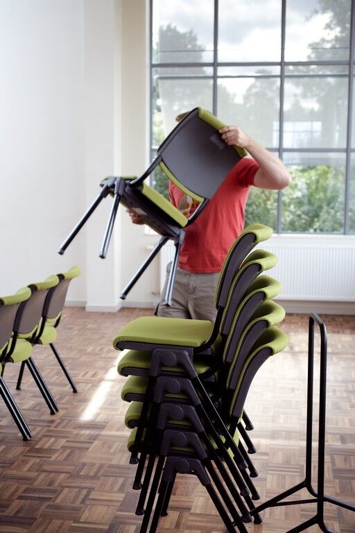 Person stapelt grüne ergonomische Stühle in einem Raum mit großen Fenstern.