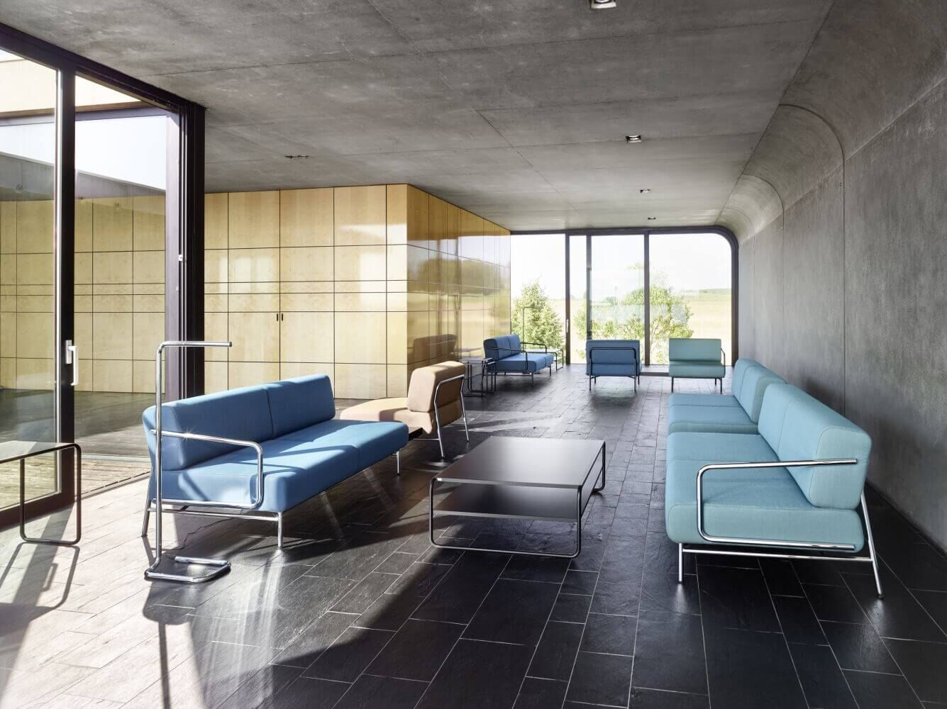 Moderne Lounge mit blauen Sofas, Glaswänden und natürlichem Lichteinfall für entspannte Atmosphäre.