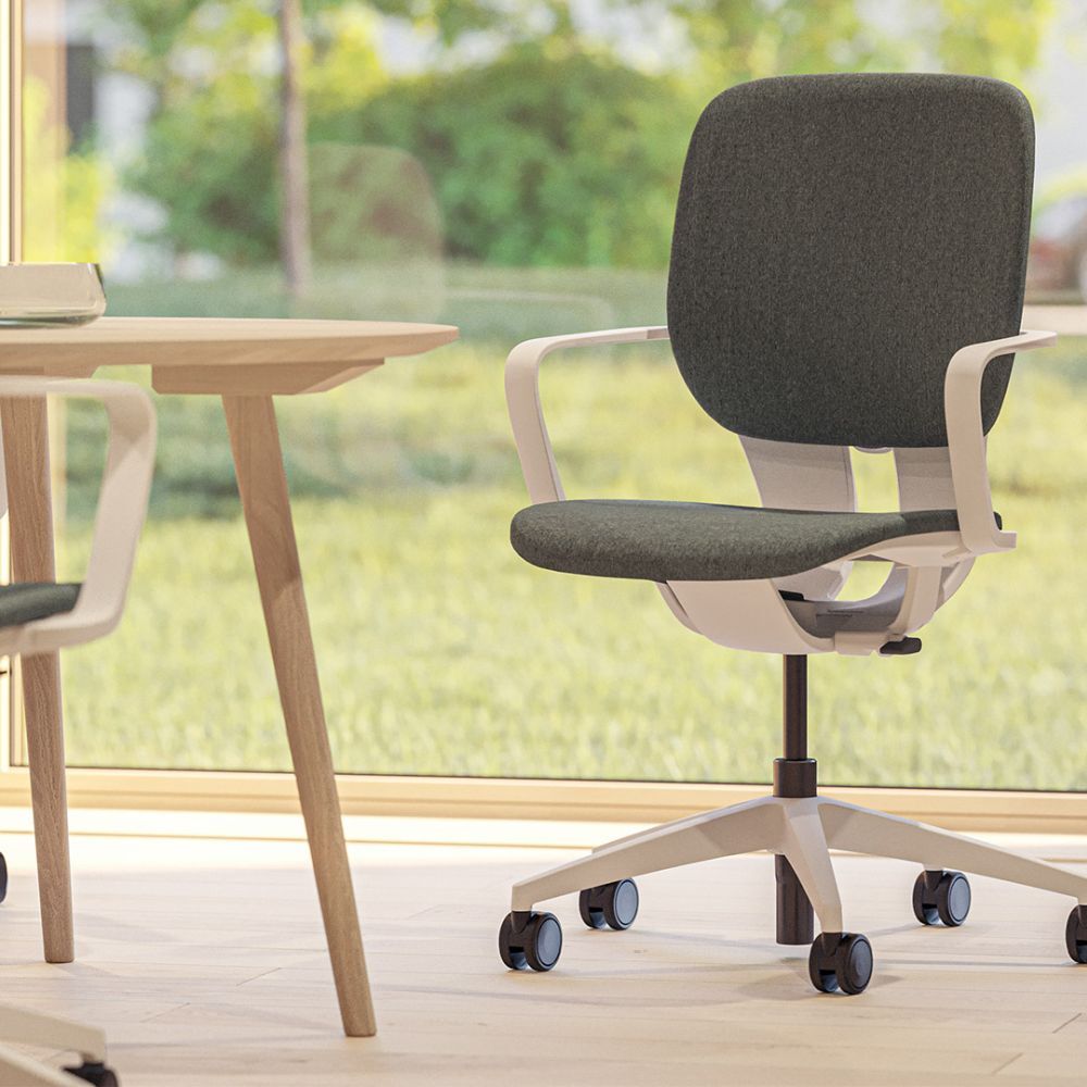 Ergonomischer Bürostuhl mit grauem Bezug und weißen Armlehnen, steht vor einem Schreibtisch, grüne Aussicht.