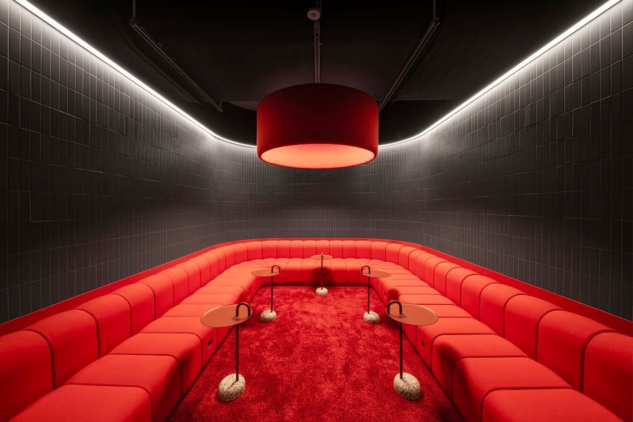 Modernes, rotes, U-förmiges Sofa in einem minimalistischen Raum mit rotem Teppich und zentraler Pendelleuchte.