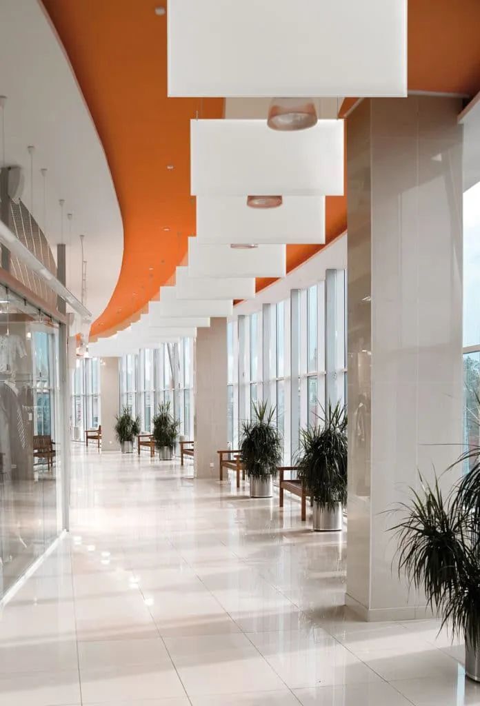 Heller Flur mit großen Fenstern, oranger Decke und Pflanzen in elegantem, modernem Eingangsbereich.