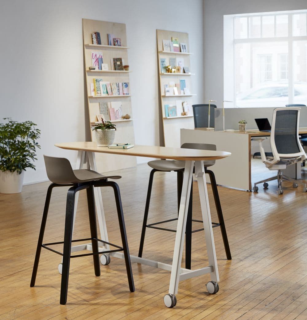 Moderne Büroumgebung mit ergonomischen Stühlen, Stehpult und Bücherregalen für gesundes, bewegtes Sitzen.