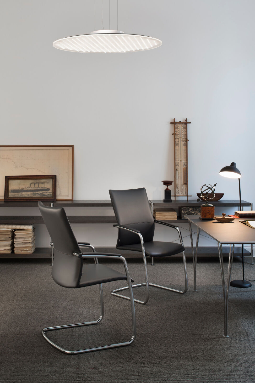 Moderner Büroraum mit eleganten schwarzen Bürostühlen, schlankem Tisch, Regalen und auffälliger Deckenleuchte.