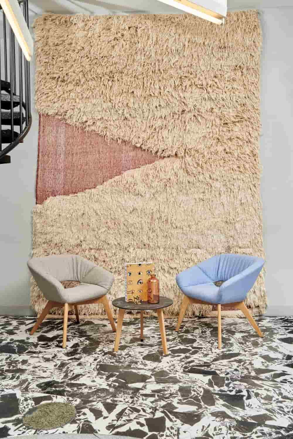 Zwei moderne Sessel und ein Tisch vor einem großen Wandteppich in einem stilvollen, gemusterten Raum.