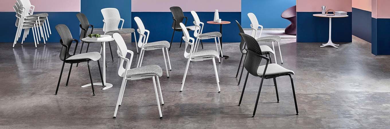 Mehrere moderne ergonomische Stühle in einem Showroom mit pastellfarbenen Wänden und grauem Boden.