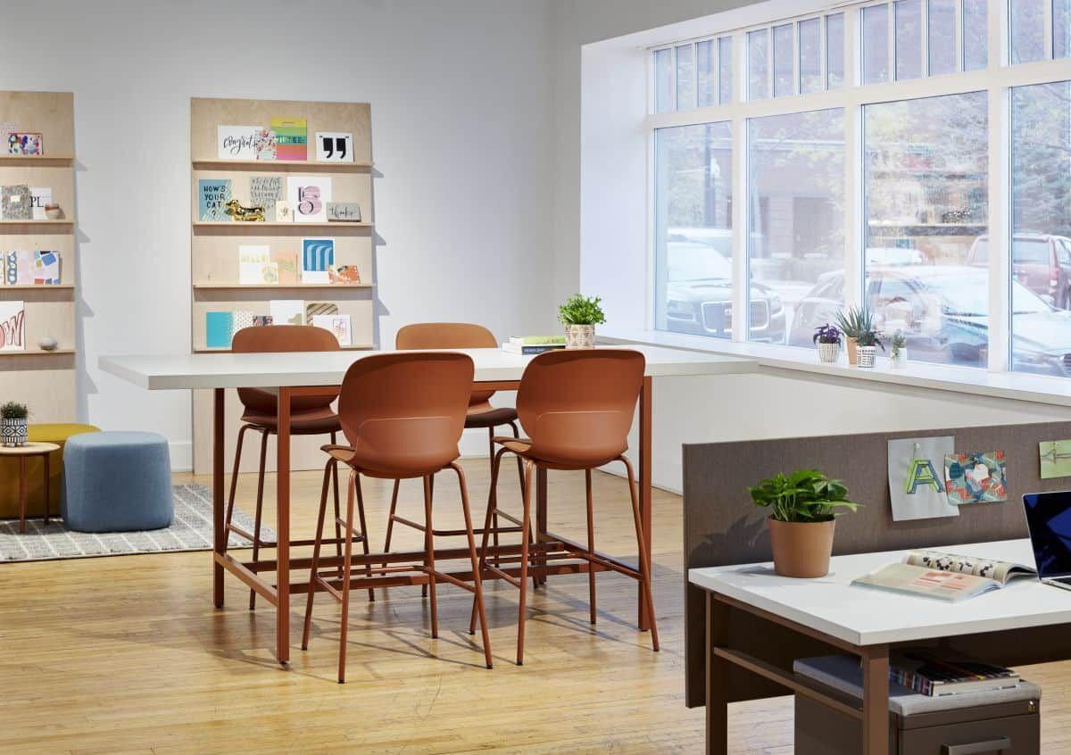 Moderner Arbeitsbereich mit hohem Tisch, ergonomischen Stühlen und viel Tageslicht aus großen Fenstern.