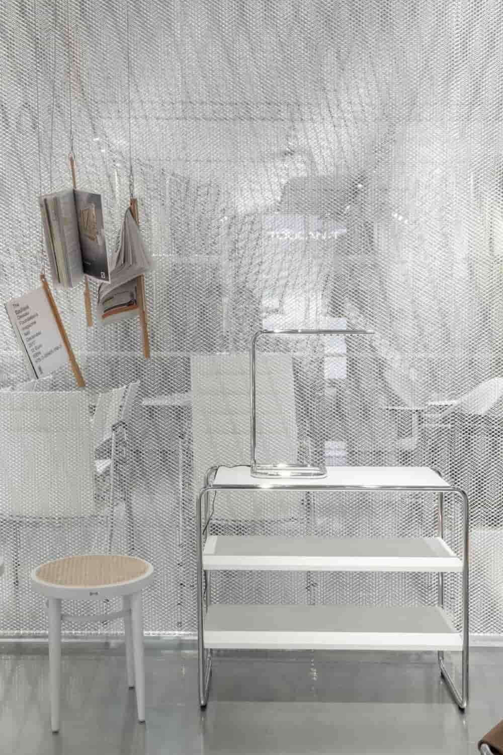 Weißer Hocker und Regal vor silbernem Netzvorhang mit hängenden Zeitschriften, modernes minimalistisches Design.