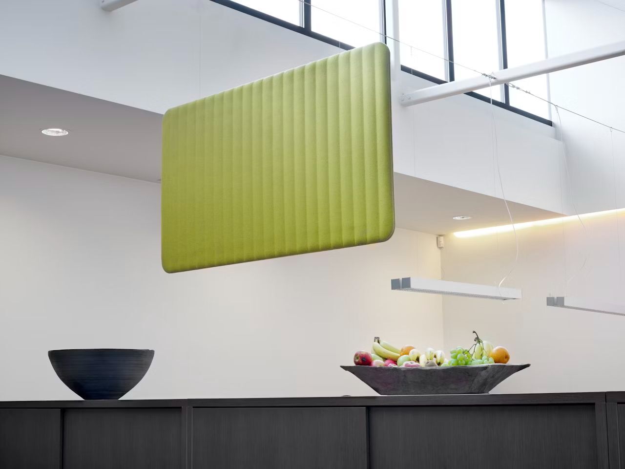 Ein modernes Büro mit grünem Akustik-Panel an der Decke und Obstschale auf dem Tisch.