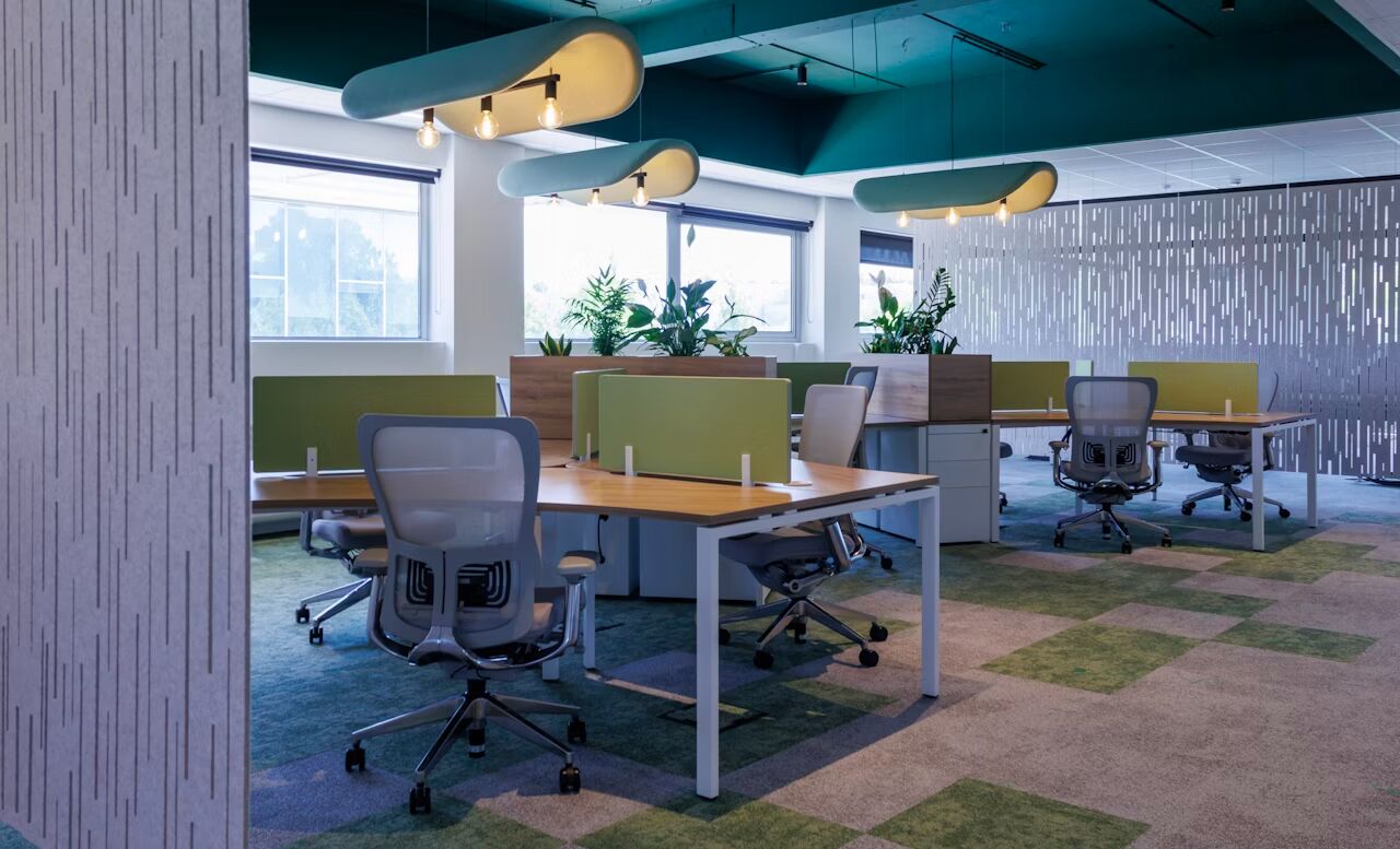 Moderner Büroraum mit ergonomischen Stühlen, Schreibtischen, grünen Trennwänden und Pflanzen, fördert gesundes Arbeiten.