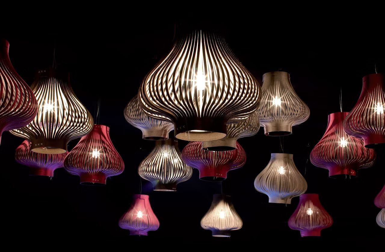 Mehrere bunte, leuchtende Lichter mit geschwungenen Linien hängen von der Decke vor einem dunklen Hintergrund.