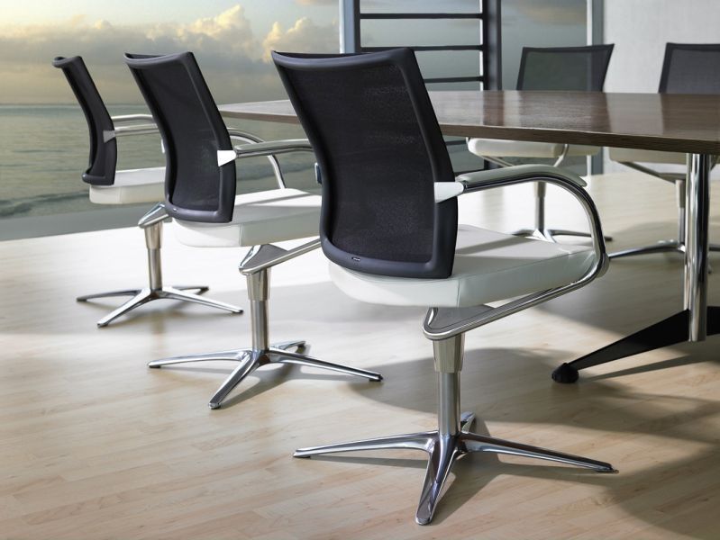 Drei ergonomische Bürostühle mit Netzrückenlehnen und Chromgestell an einem Konferenztisch mit Meerblick.