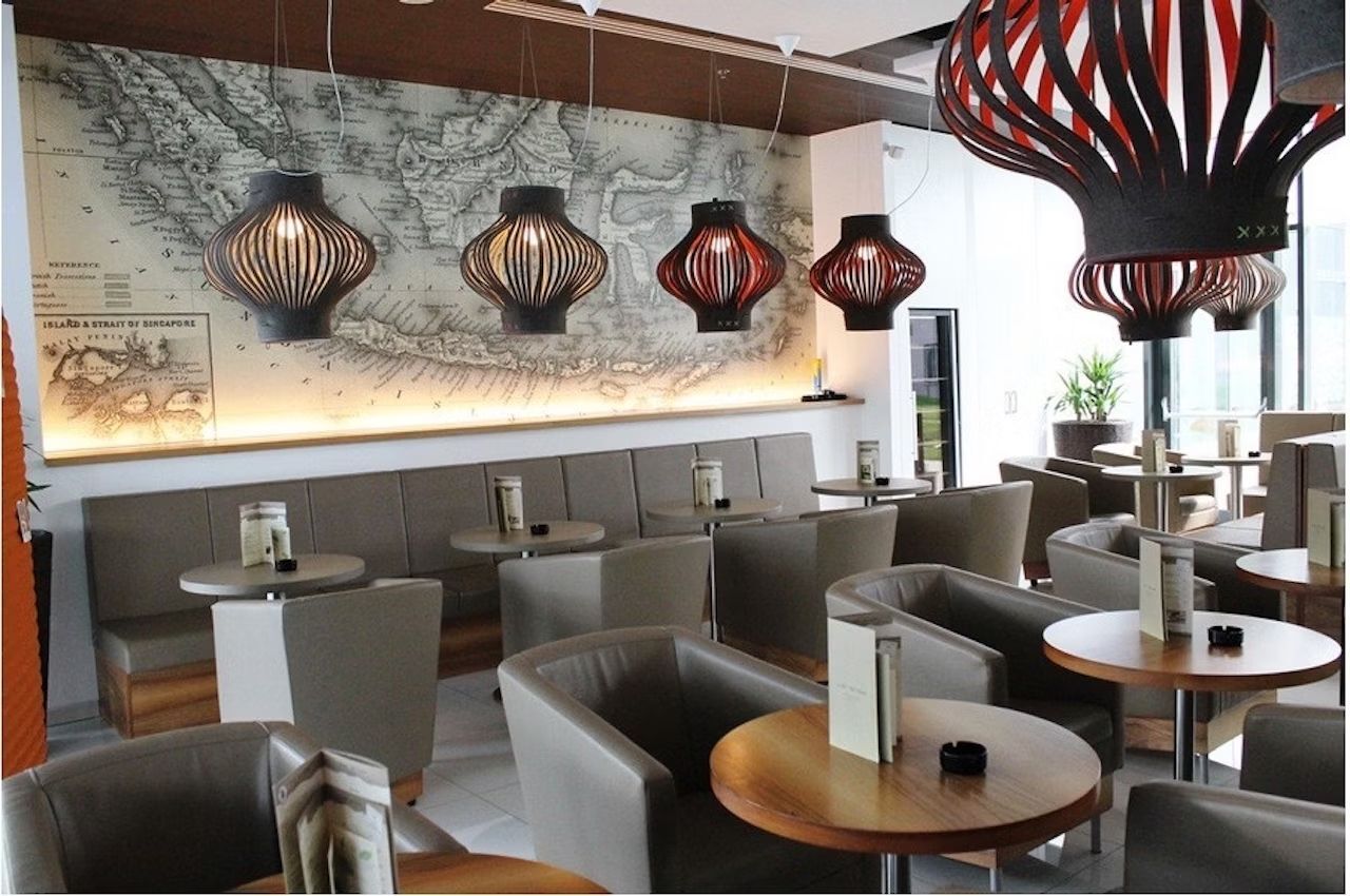 Eleganter Loungebereich mit stilvollen Hängelampen, modernen Sesseln und runden Holztischen vor historischer Karte.