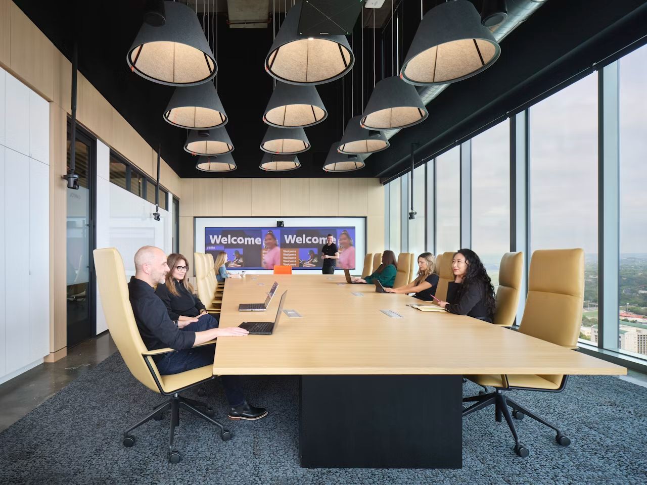 Menschen in einem modernen Besprechungsraum mit Blick auf Stadtlandschaft, ergonomische Stühle und große Bildschirme.