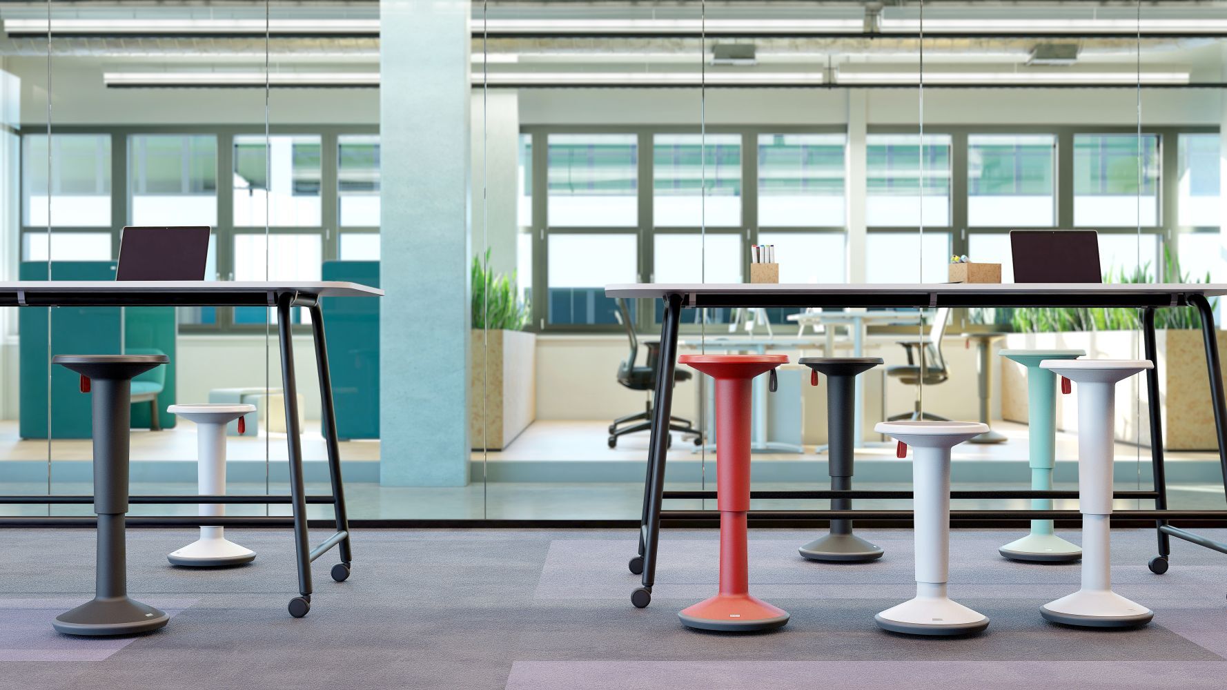 Ergonomische Hocker in verschiedenen Farben vor einem modernen Bürorahmen mit Laptop auf verstellbarem Tisch.